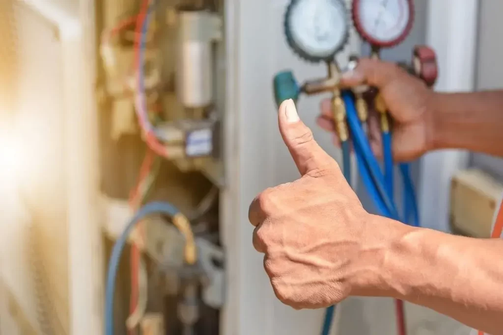 Person giving a thumbs-up while holding air conditioning gauges, indicating successful maintenance or repair work.